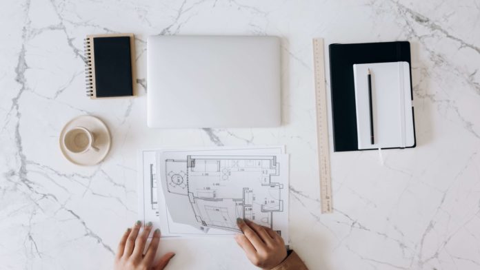 floor plans laid on white marble benchtop with laptop, coffee, notebook.