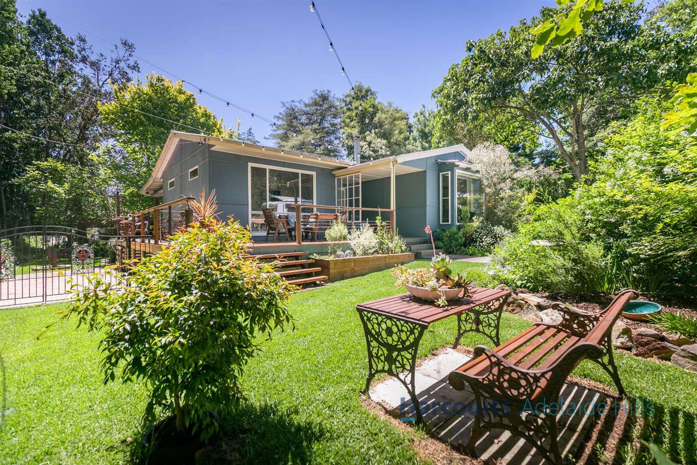 Backyard of blue house with lawn, trees bench and table
