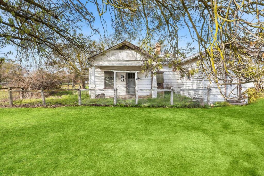 home in Victoria front yard with green lawn and trees shading the front of the white weatherboard house