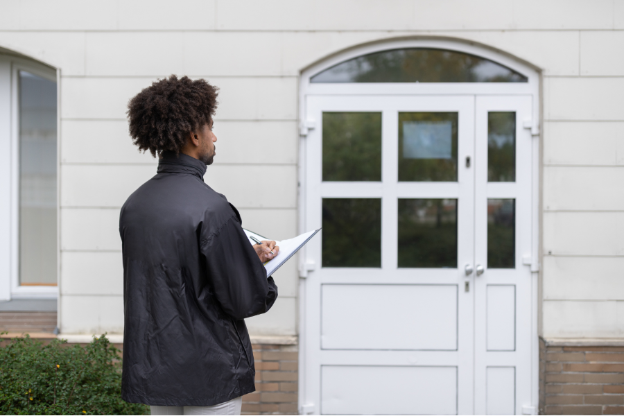 Person standing in front of house entrance with clipboard